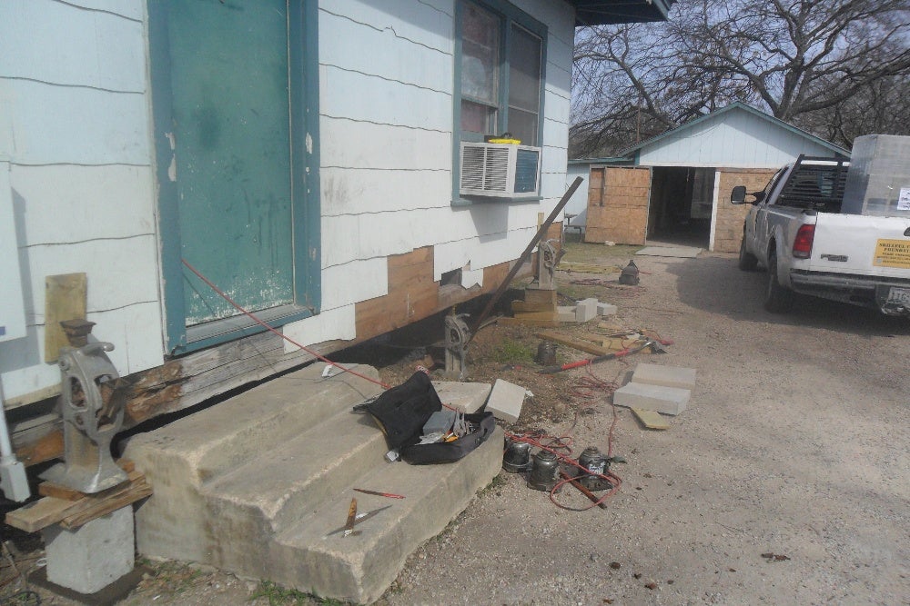 Home undergoing foundation repair, showing jacks and tools outside